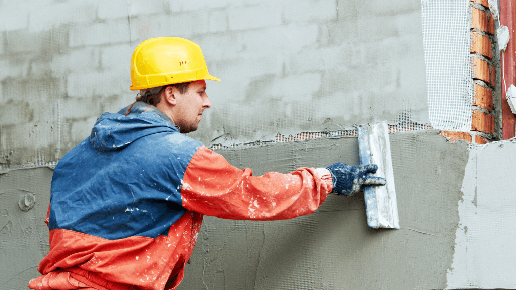 Plasterer in a hard hat applying render to a brick wall with a trowel